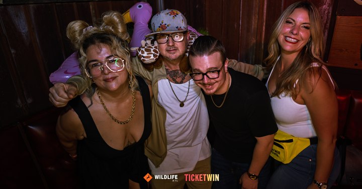 Four friends crowded together for a photo, one of them wearing an inflatable flamingo