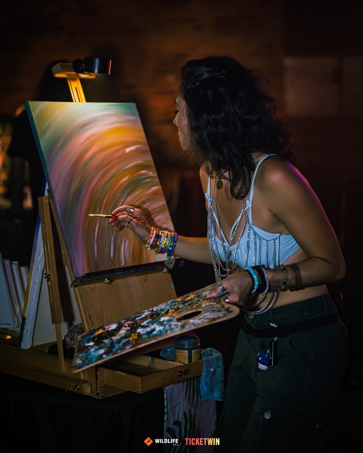 A painter working at an easel beside the dancefloor, palette in hand