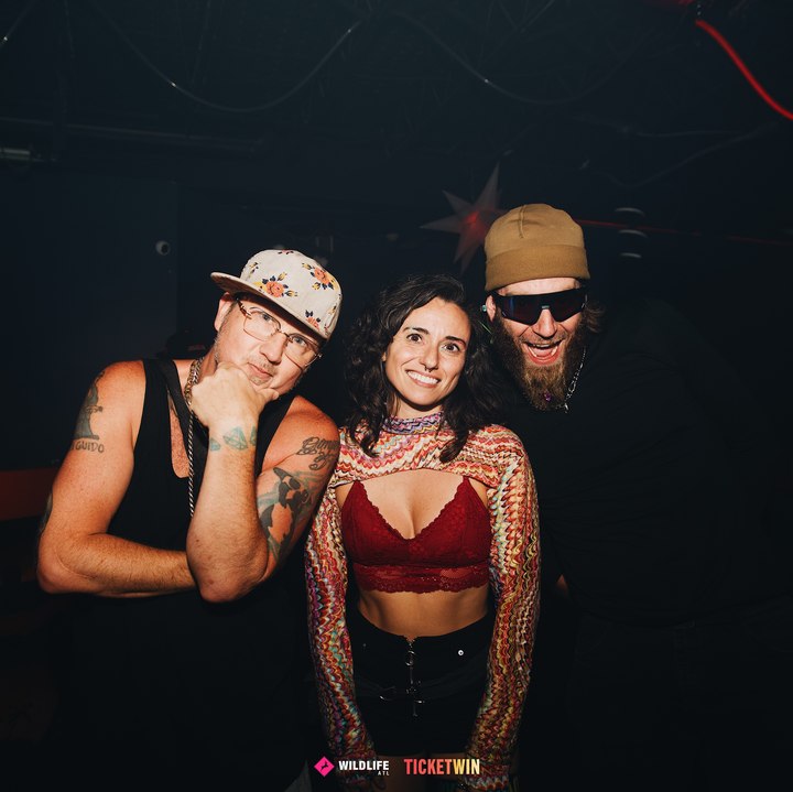Three friends posing together for the camera against the club's red padded wall