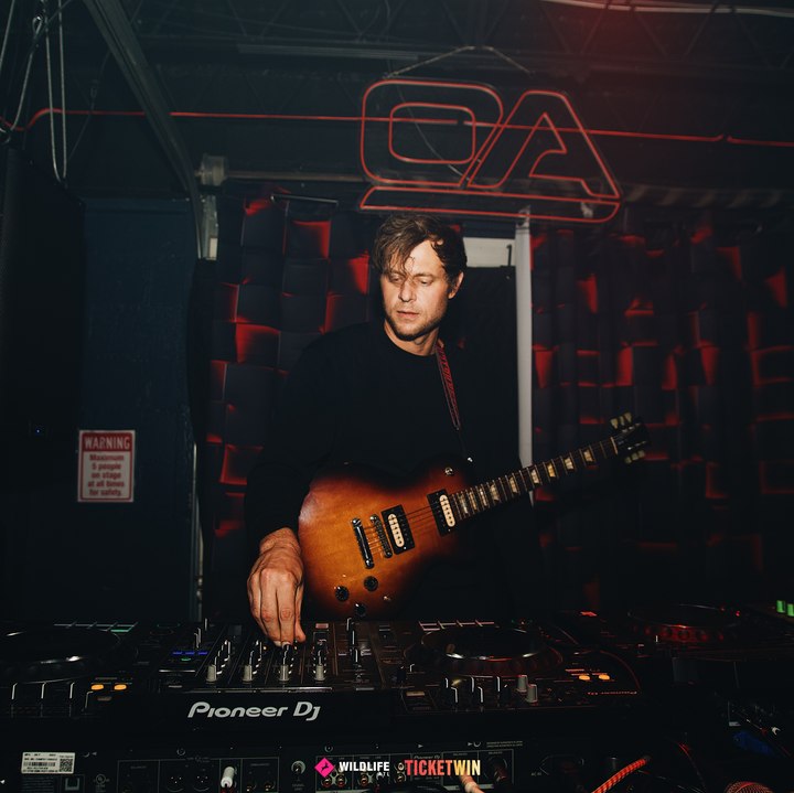 A guitarist playing live over the decks, leaning into the mixer