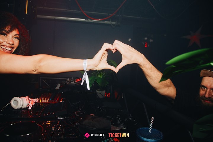 Two people reaching across the booth to make a heart with their hands, one of them laughing